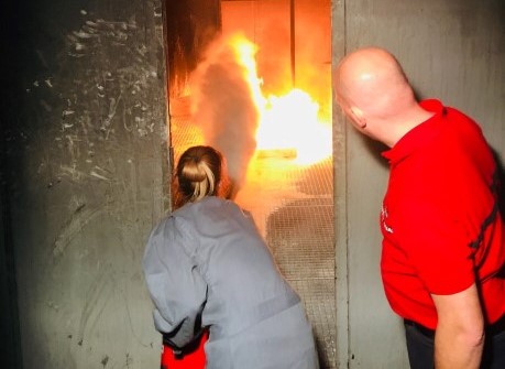 Crew member practicing firefighting technique during a training fire drill, without full PPE